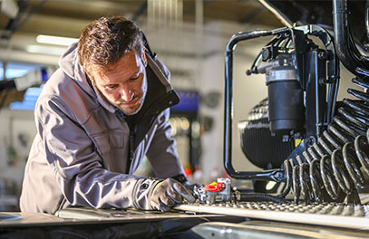 Eine Person arbeitet an einer industriellen Maschine und nimmt Einstellungen oder Wartungsarbeiten vor. Die Produktionshalle ist mit technischen Geräten und Metallanlagen ausgestattet.